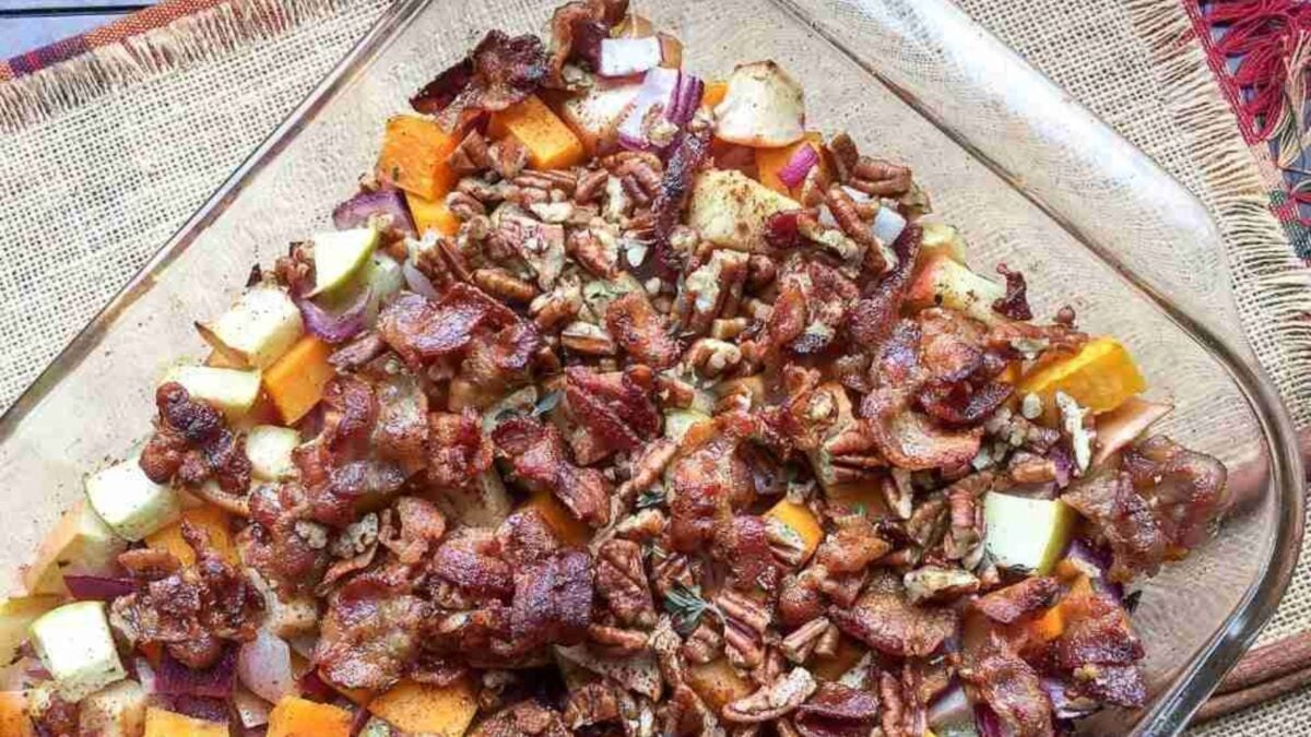 Glass dish with a baked mixture of diced sweet potatoes, apples, onions, pecans, and crispy bacon.