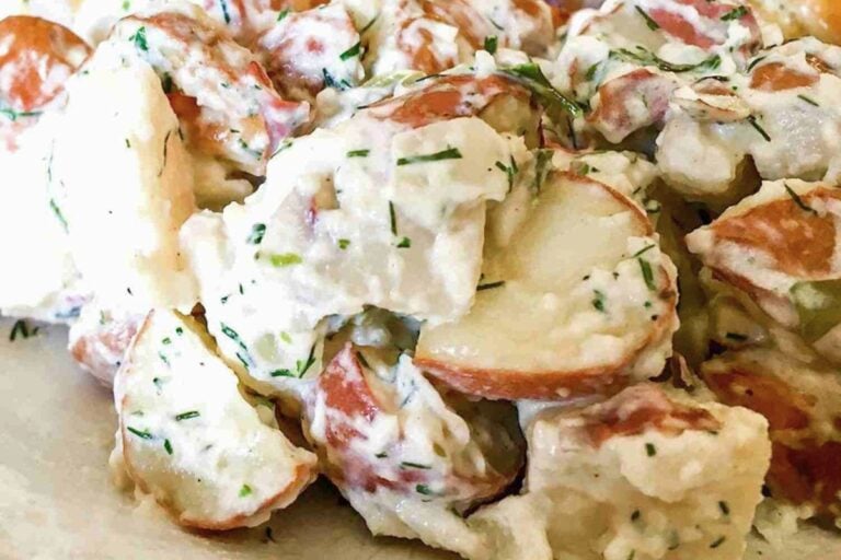 Close-up of creamy potato salad with chopped red potatoes, mayonnaise dressing, and fresh herbs.