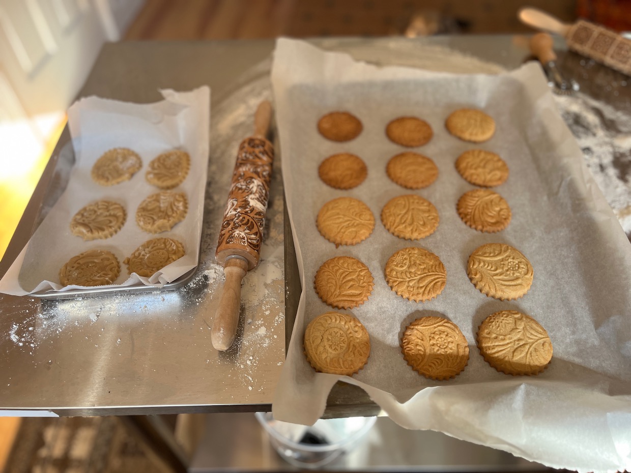 Eight embossed round cookies on a parchment-lined baking sheet. The cookies feature intricate floral and leaf patterns.