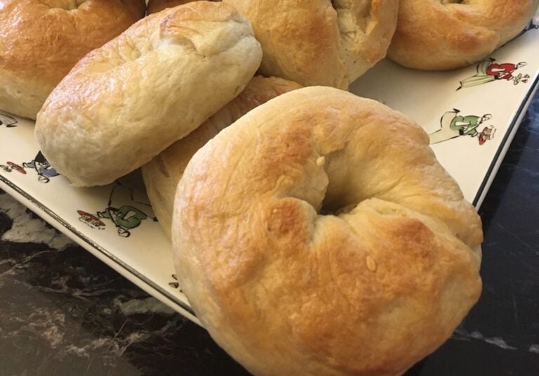 A stack of New York bagels rests on a decorative tray, their iconic shape and taste highlighted by the elegant marble surface beneath.