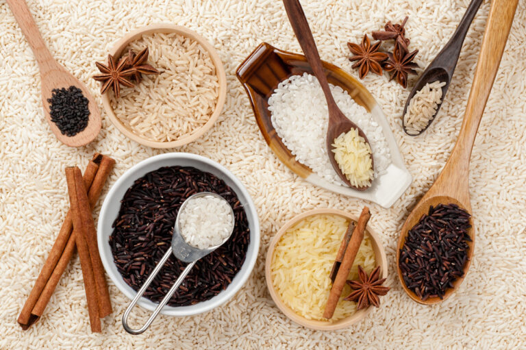 An exquisite showcase of types of rice with wooden spoons and bowls, featuring white, black, and brown varieties. Cinnamon sticks and star anise are artfully scattered among the rice for a touch of aromatic elegance.
