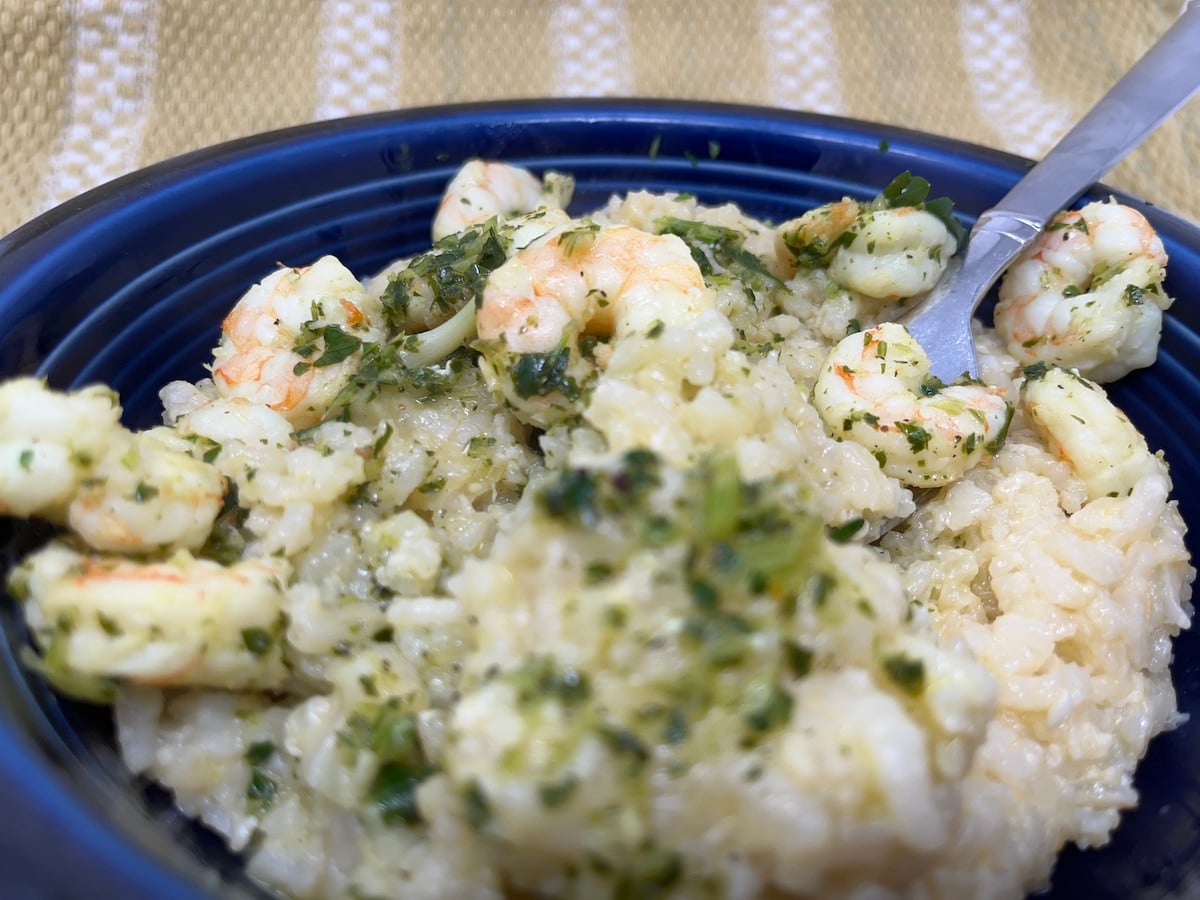 A close-up of shrimp risotto garnished with herbs in a blue bowl, with a spoon.