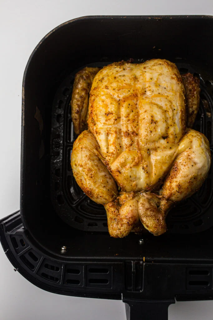 A whole chicken in an air fryer basket, seasoned and ready to be cooked.