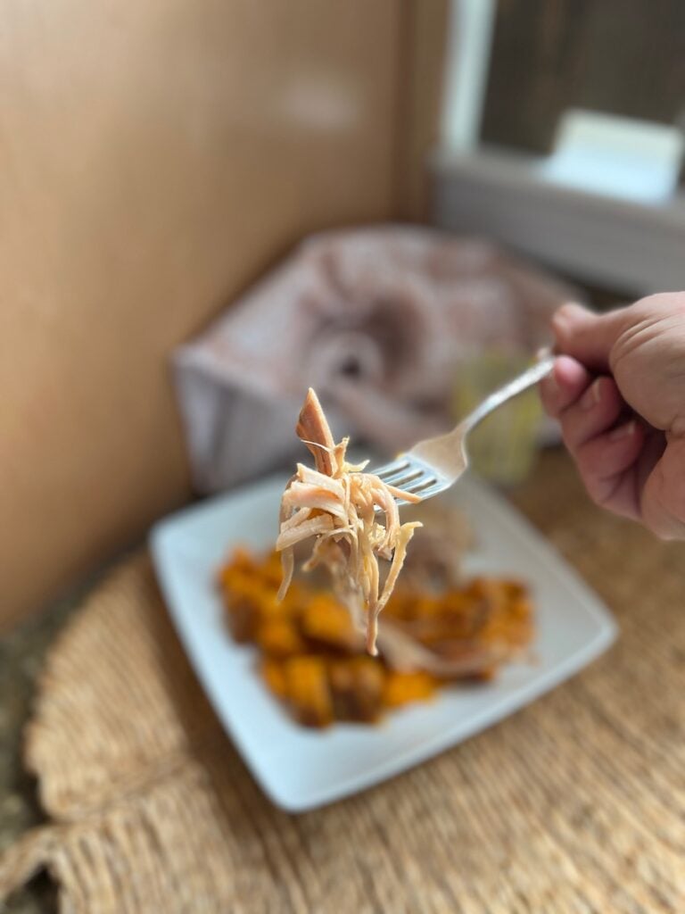 A person holding a fork with a bite of chicken and roasted vegetables on a white plate, with a blurred background.
