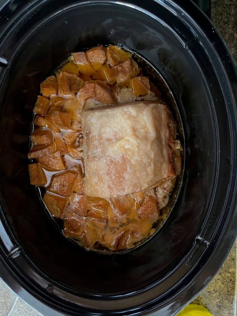 Pork roast cooking in a slow cooker with a brown sauce, viewed from above.