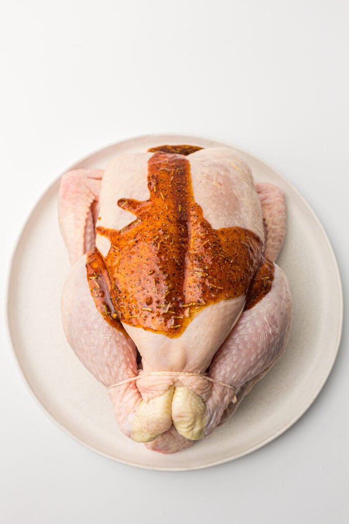 Whole chicken in air fryer with seasoning on a plate, ready for cooking, on a white background.