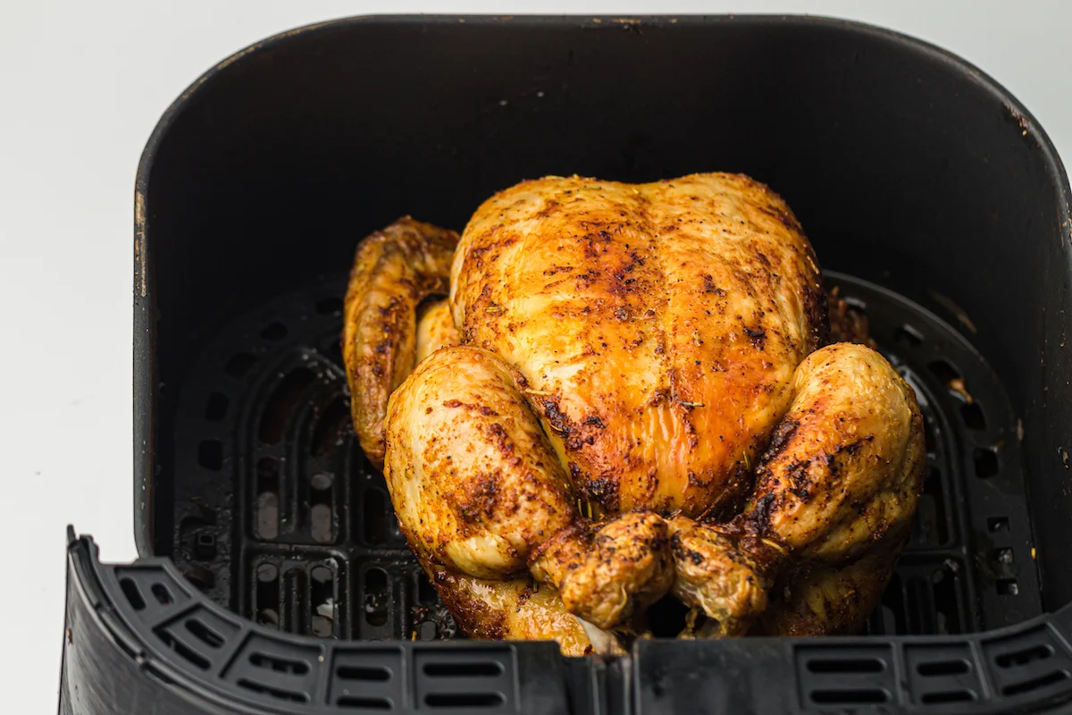 A golden-brown whole chicken in a black air fryer basket against a white background.