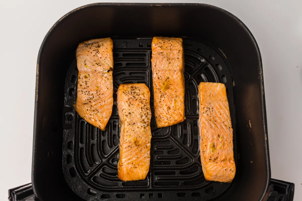 Four seasoned salmon fillets placed in a black air fryer basket, seen from above.