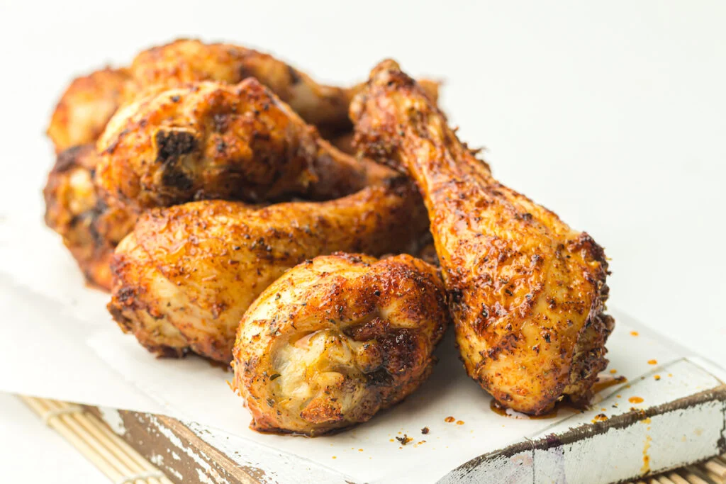 A stack of seasoned and cooked chicken drumsticks on a white surface.