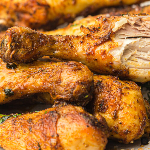 A close-up of cooked chicken drumsticks seasoned with spices, one partially eaten to reveal the white meat inside.