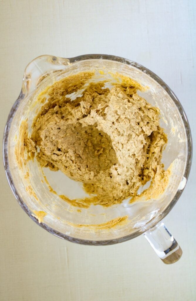 A top view of a glass mixing bowl containing thick, partially mixed dough.