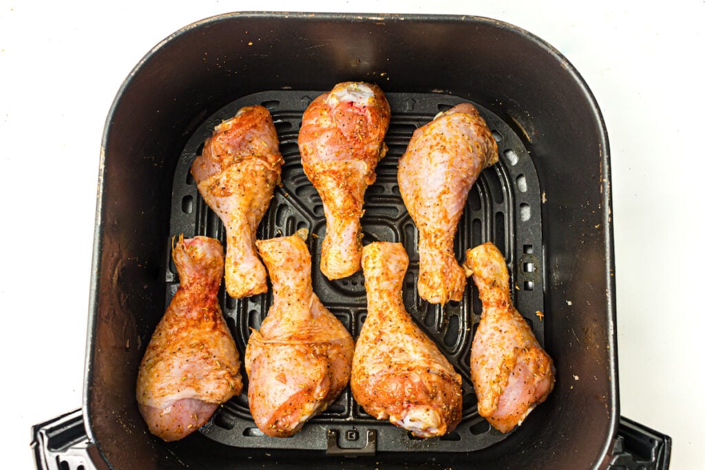 Six seasoned chicken drumsticks arranged in an air fryer basket, ready for cooking.