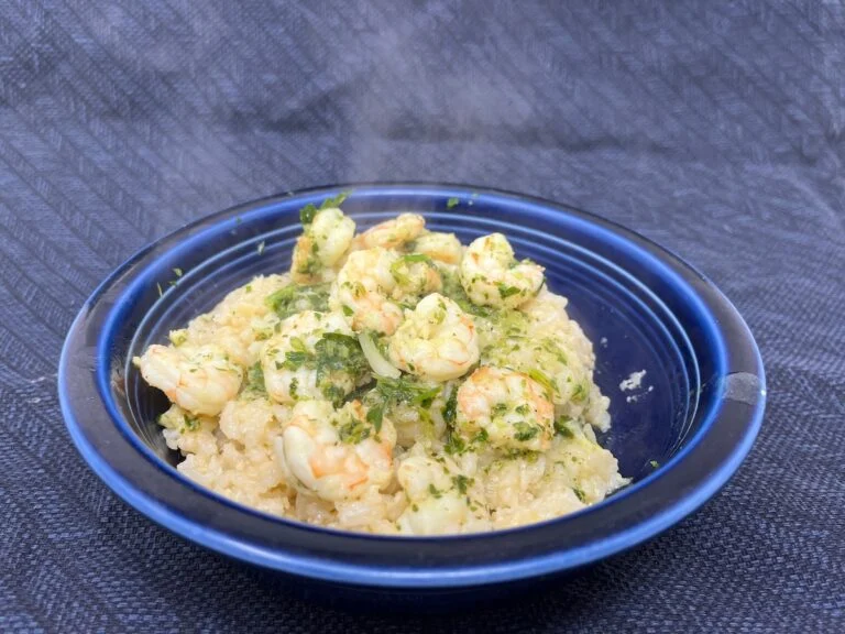 A blue bowl filled with shrimp risotto garnished with herbs is placed on a textured dark surface.