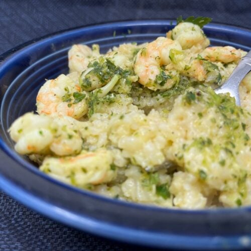 A blue bowl containing rice and shrimp mixed with a green herb sauce, with a fork placed in the dish.