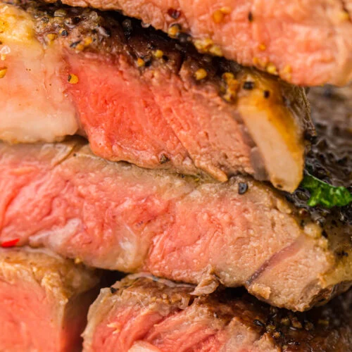 Close-up of medium-rare grilled steaks stacked on top of each other, showing a pink interior and seasoned crust.