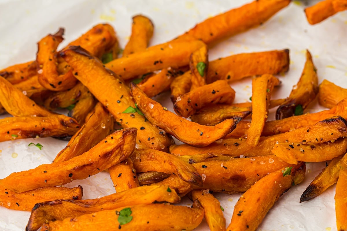Close-up of a pile of seasoned sweet potato fries garnished with small green herbs, served on a white plate—perfect for celebrating National French Fry Day.