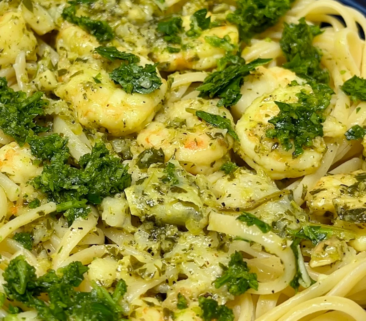 A blue bowl filled with shrimp and rice, topped with green herbs, with a metal spoon in the bowl.