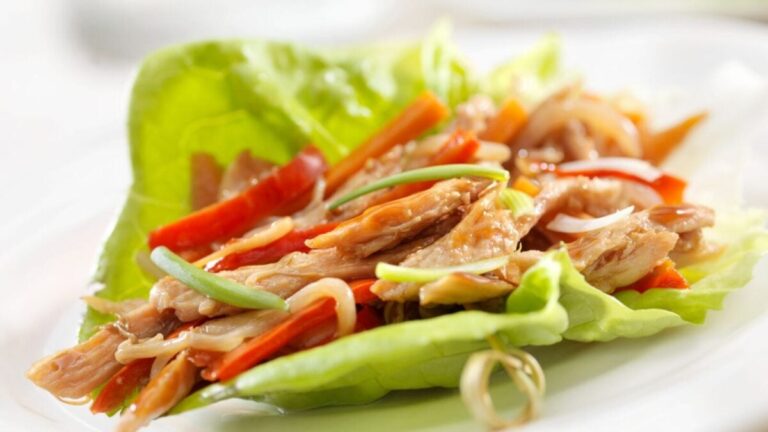 Lettuce wrap with shredded chicken, sliced red peppers, and green onions on a white plate.