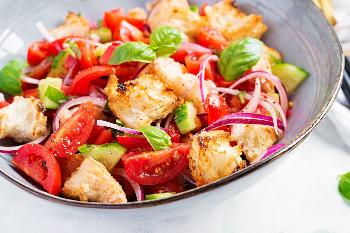 A bowl of panzanella salad with tomatoes, cucumbers, red onions, croutons, and basil leaves.