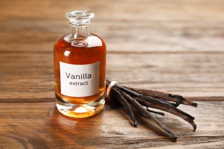 A glass bottle labeled "Vanilla extract" is placed next to a few vanilla beans on a wooden surface.