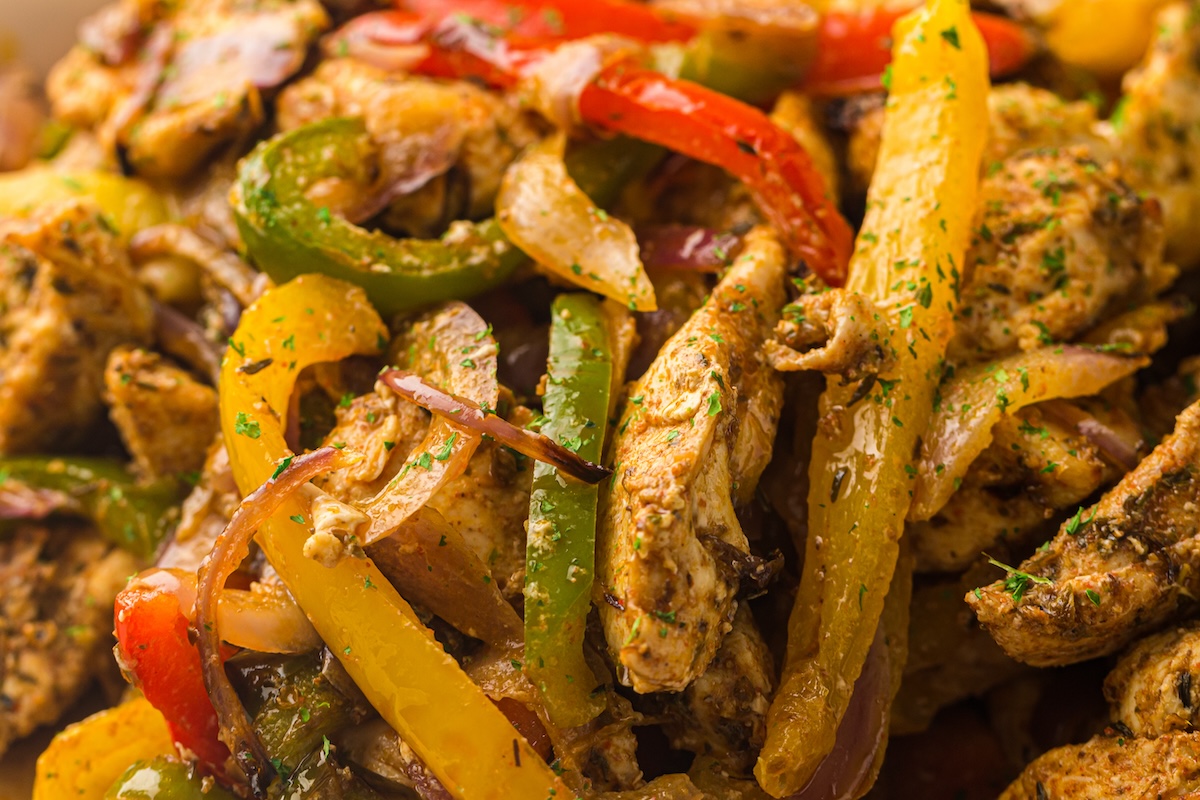 A close-up of a vibrant stir-fry dish featuring air fryer chicken fajitas with seasoned chicken, yellow, green, and red bell peppers, and onions.
