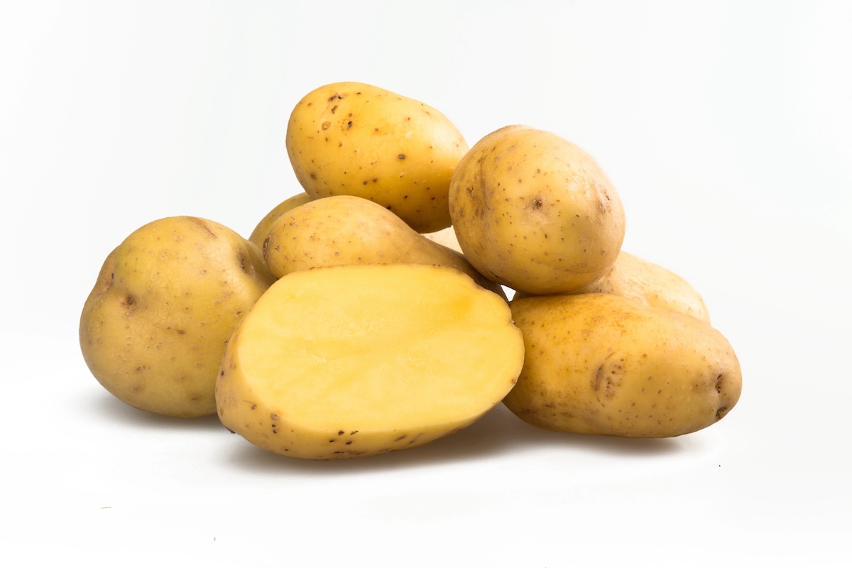 A pile of whole yellow potatoes with one potato cut in half, revealing the inside. The background is plain white.