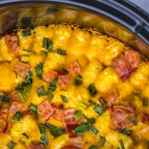 Top view of a cheesy casserole with bacon pieces and chopped green onions in a black dish.
