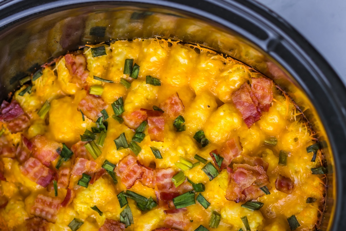Top view of a cheesy casserole with bacon pieces and chopped green onions in a black dish.
