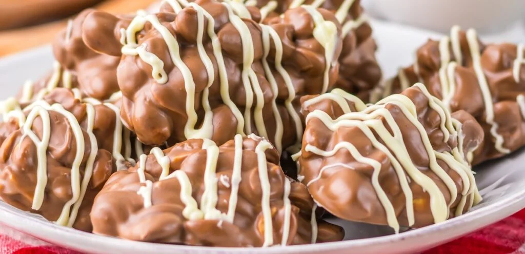 A plate of Crock Pot Chocolate Nut Clusters drizzled with elegant white chocolate lines.