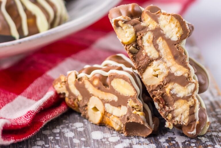 Close-up of two chunks of nutty chocolate bark with nuts visible, reminiscent of crock pot chocolate nut clusters, placed on a red checkered cloth and a wooden surface.