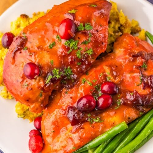 A plate of slow cooker cranberry chicken, featuring stuffed breasts adorned with tart cranberries, served alongside tender green beans and fluffy rice, all elegantly garnished with fresh parsley.