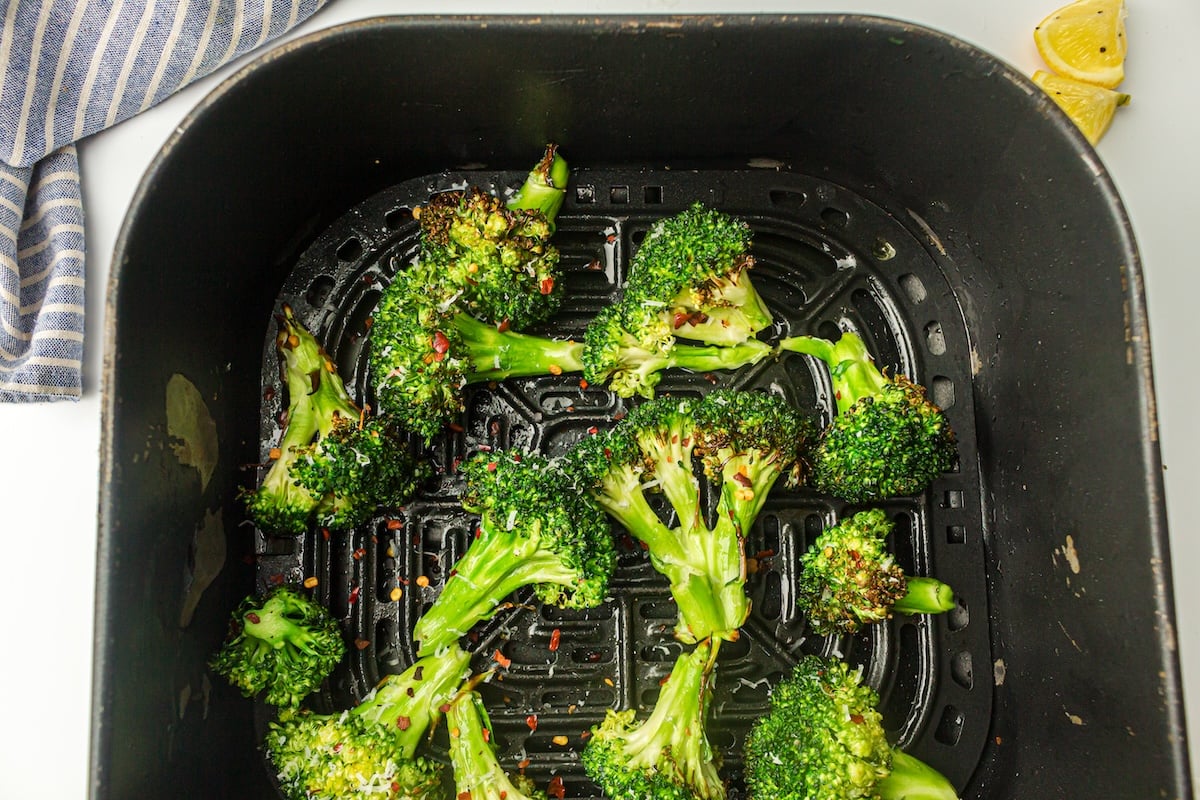 Air fryer broccoli florets seasoned with red pepper flakes, perfectly cooked and complemented by a lemon wedge, rest on a striped cloth nearby.