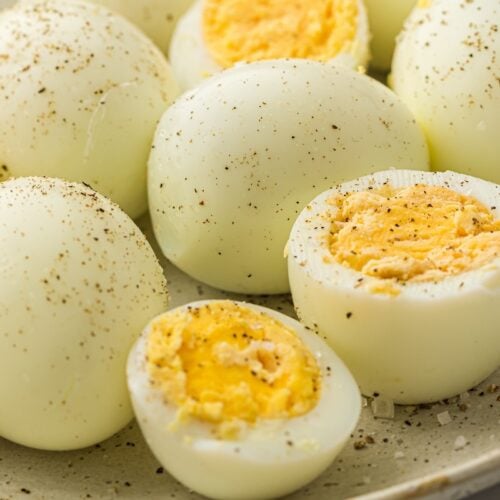 Hard-boiled eggs sliced open, seasoned with black pepper, displayed on a beige plate.