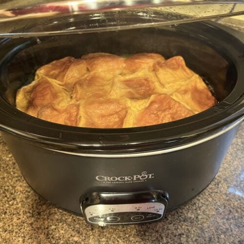 A Crock-Pot filled with golden-brown baked biscuits. The lid is partially open, showing the evenly cooked tops.