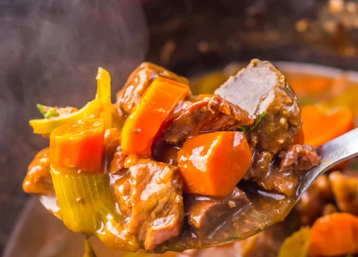 Close-up of a spoonful of slow cooker beef stew with tender chunks of beef, carrots, and celery immersed in a rich, steaming broth.