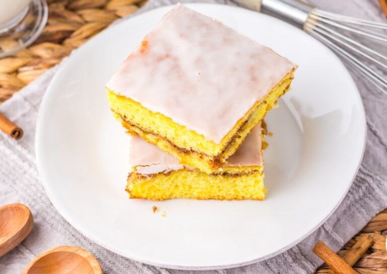Two pieces of frosted yellow cake with cinnamon swirl stacked on a white plate.