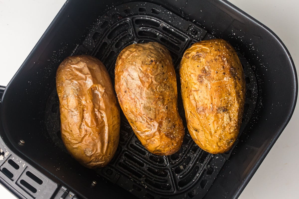 Three air fryer baked potatoes rest in the basket, perfectly seasoned and cooked to a golden brown.