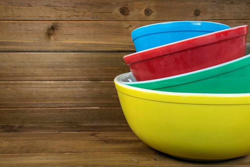 Three stacked bowls in yellow, green, red, and blue on a wooden background.
