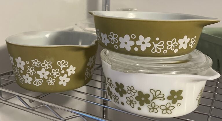 Three vintage Pyrex ceramic bowls adorned with white floral patterns are elegantly stacked on a metal shelf.