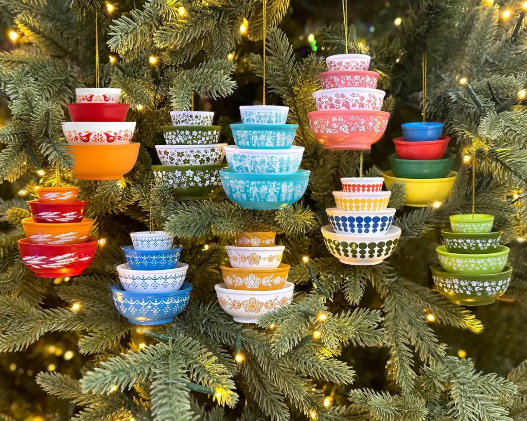 Vintage Pyrex bowls, stacked and decorated, hang as ornaments from a Christmas tree with warm white lights.
