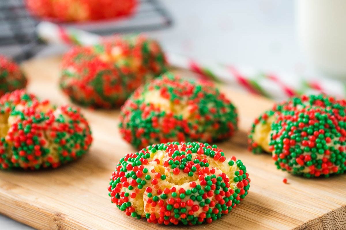 Cookies covered with red and green sprinkles are arranged on a wooden board.