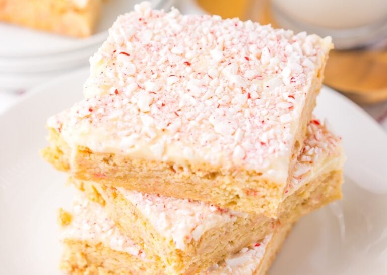 A stack of three peppermint rice krispie treats on a white plate. The treats are topped with crushed peppermint candy.