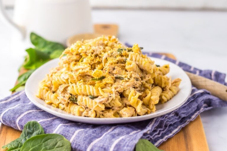 A plate of creamy pasta topped with herbs and spices, set on a striped cloth with spinach leaves nearby.
