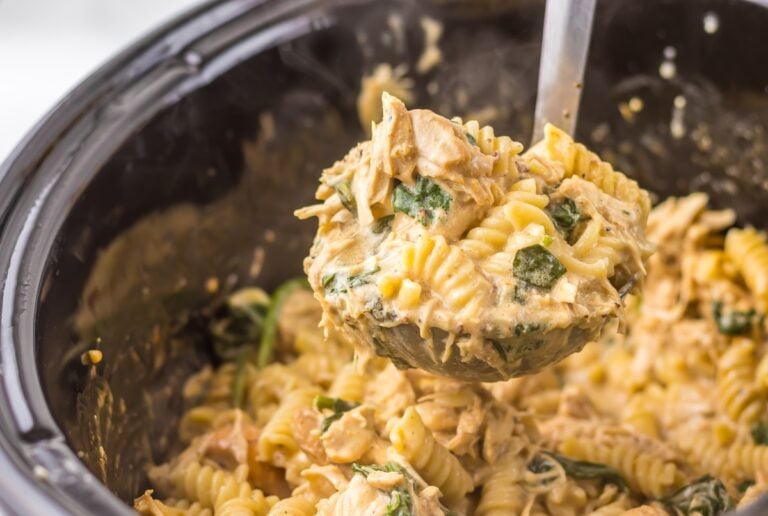 A ladle serving creamy chicken pasta with fusilli and spinach from a pot.