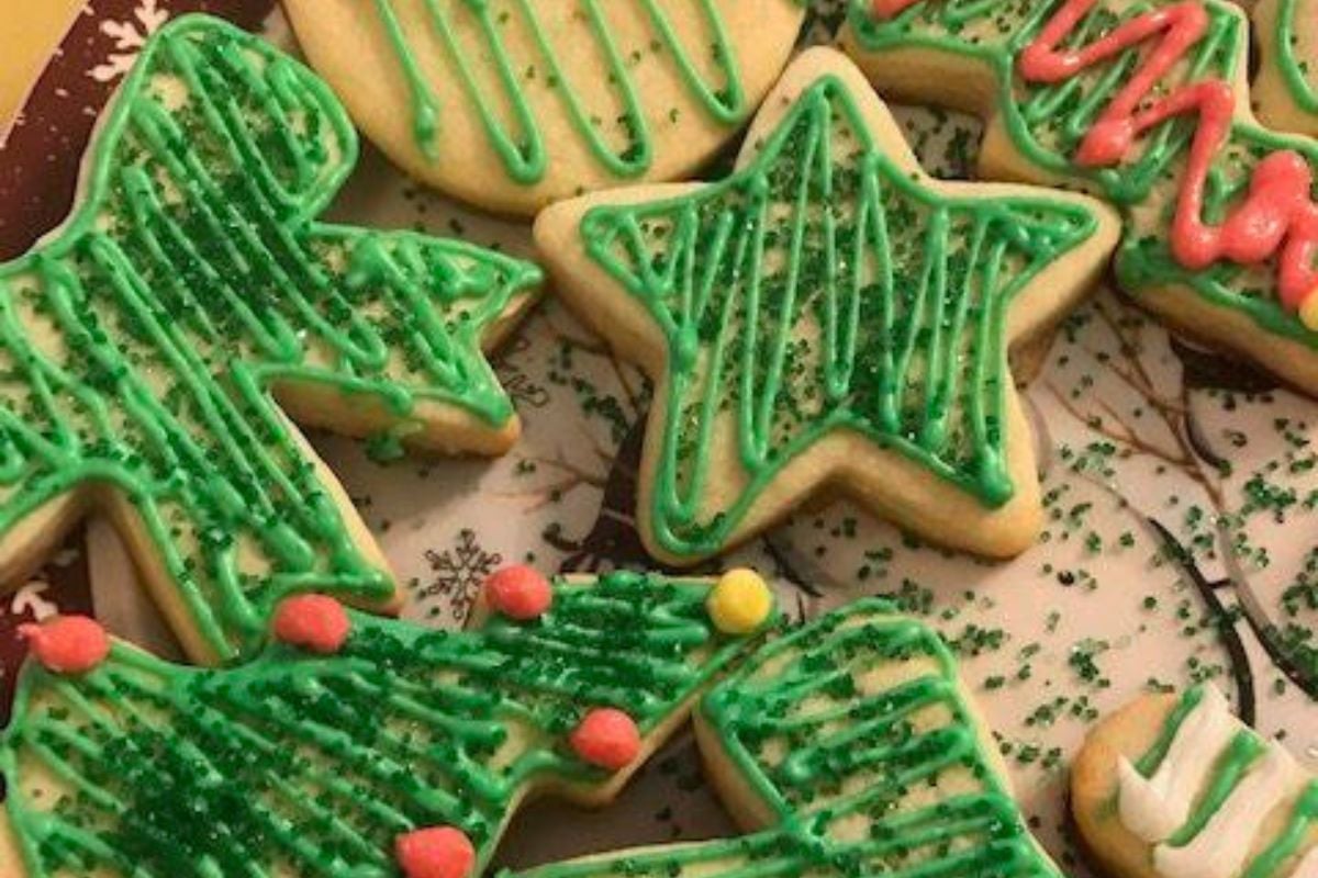 Christmas-themed cookies with green icing and sprinkled decorations, shaped like trees and stars, placed on a plate.
