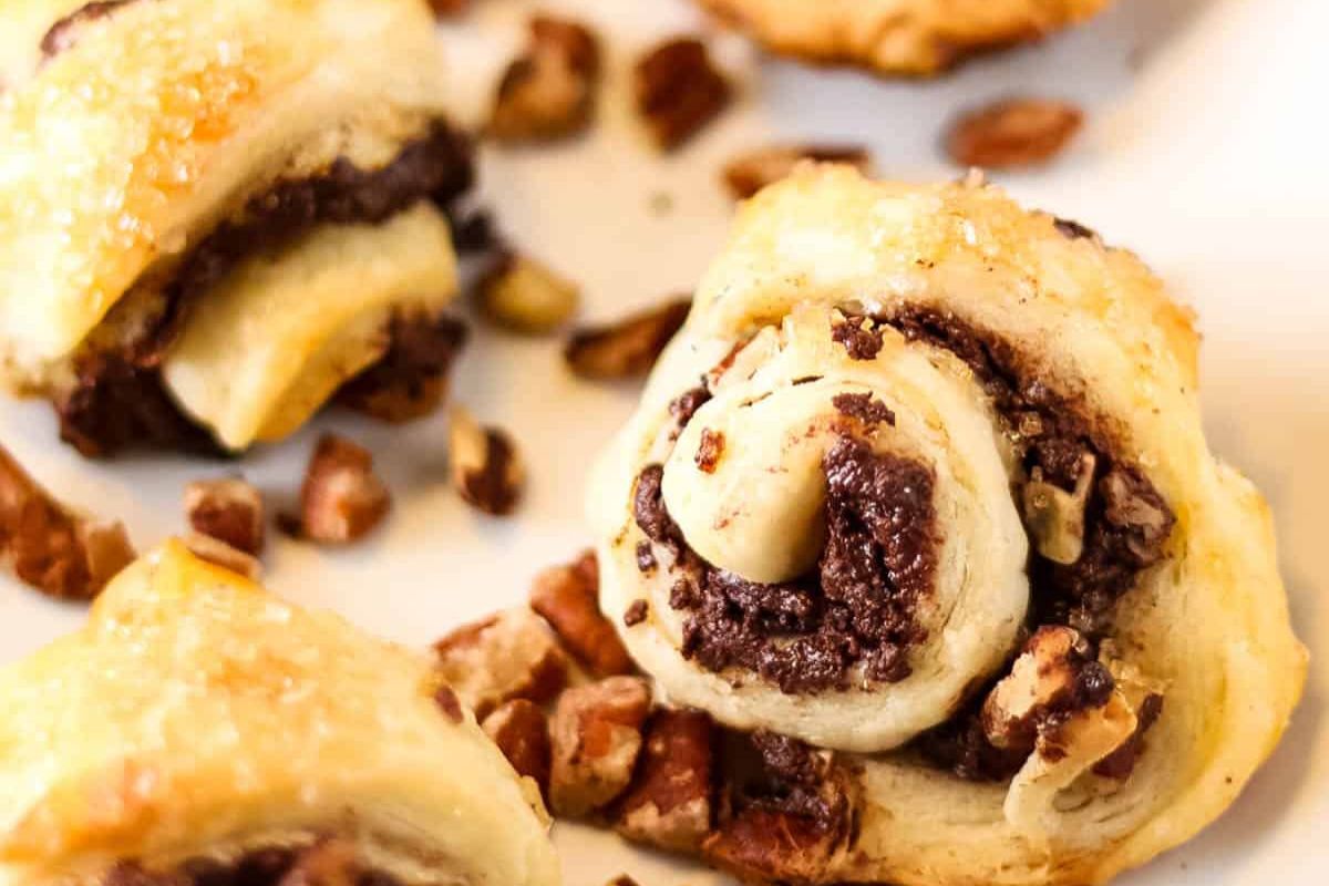 Close-up of spiral-shaped pastries with chocolate filling, surrounded by chopped nuts on a white background.