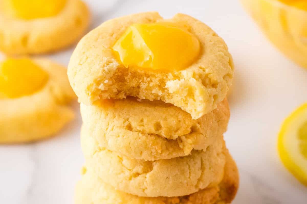 A stack of lemon thumbprint cookies with one cookie on top partially bitten.