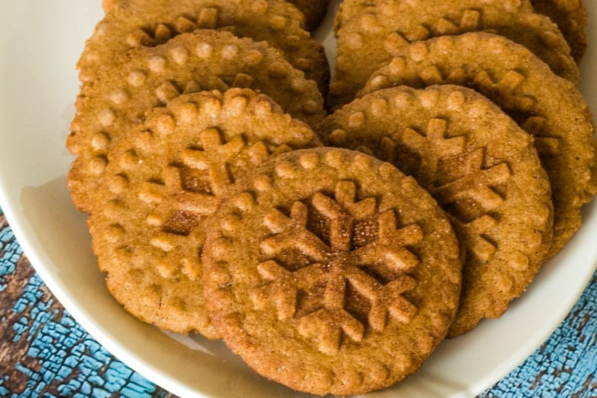 A plate of brown cookies with snowflake patterns on a blue textured surface.