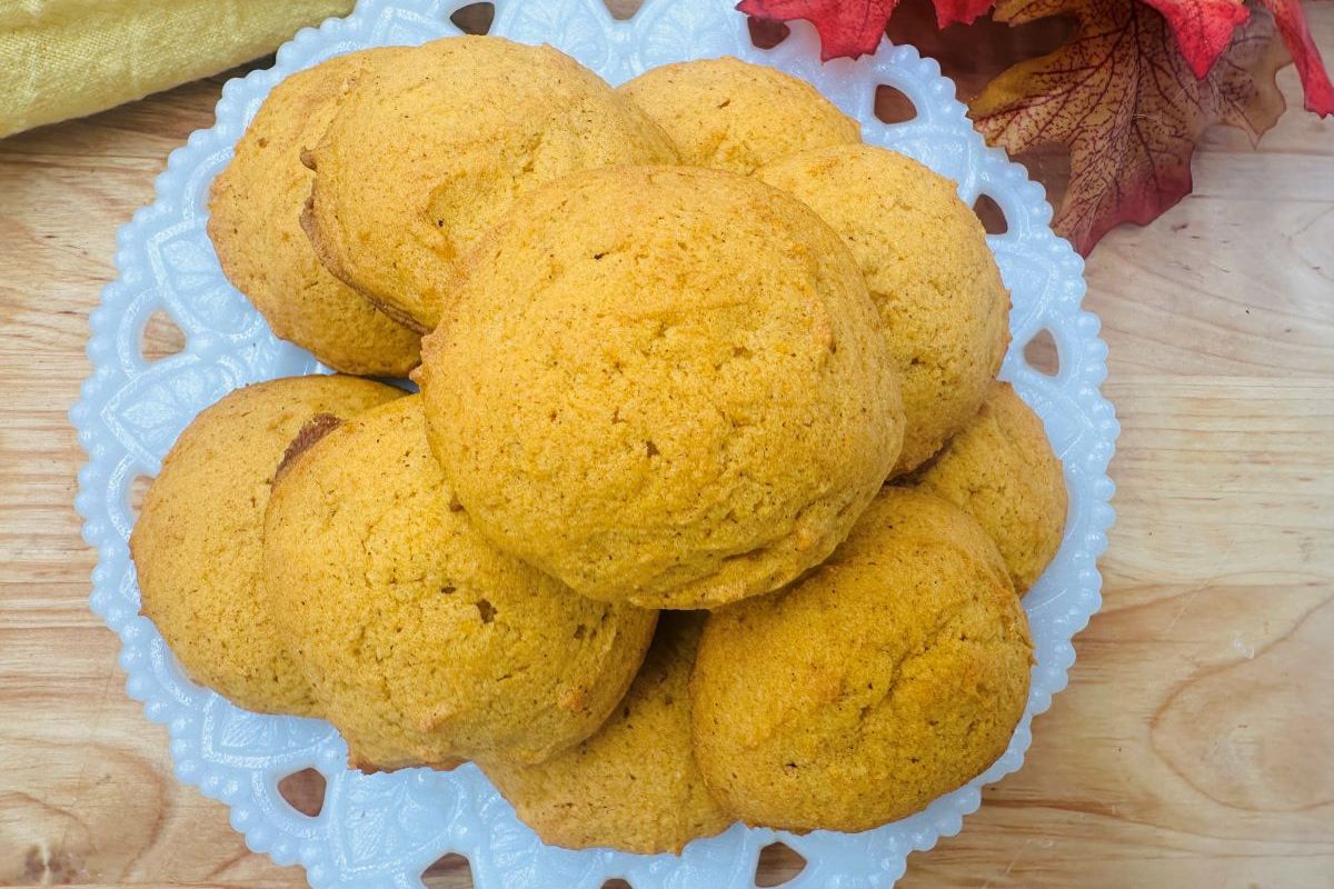 A plate of round, golden-brown cookies on a wooden table, next to autumn leaves.