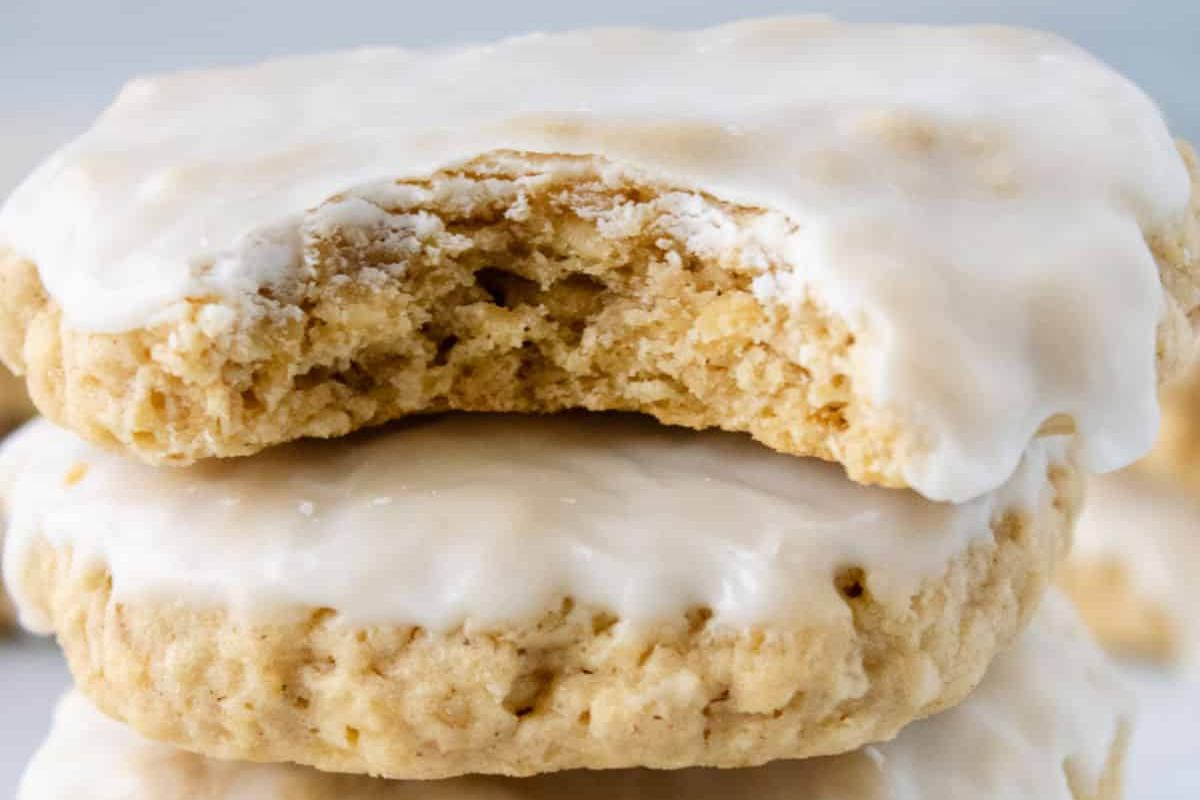Two iced oatmeal cookies stacked, the top cookie has a bite taken out, revealing a soft, chewy interior.